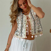 Woman wearing an embroidered top with tassels against a neutral background